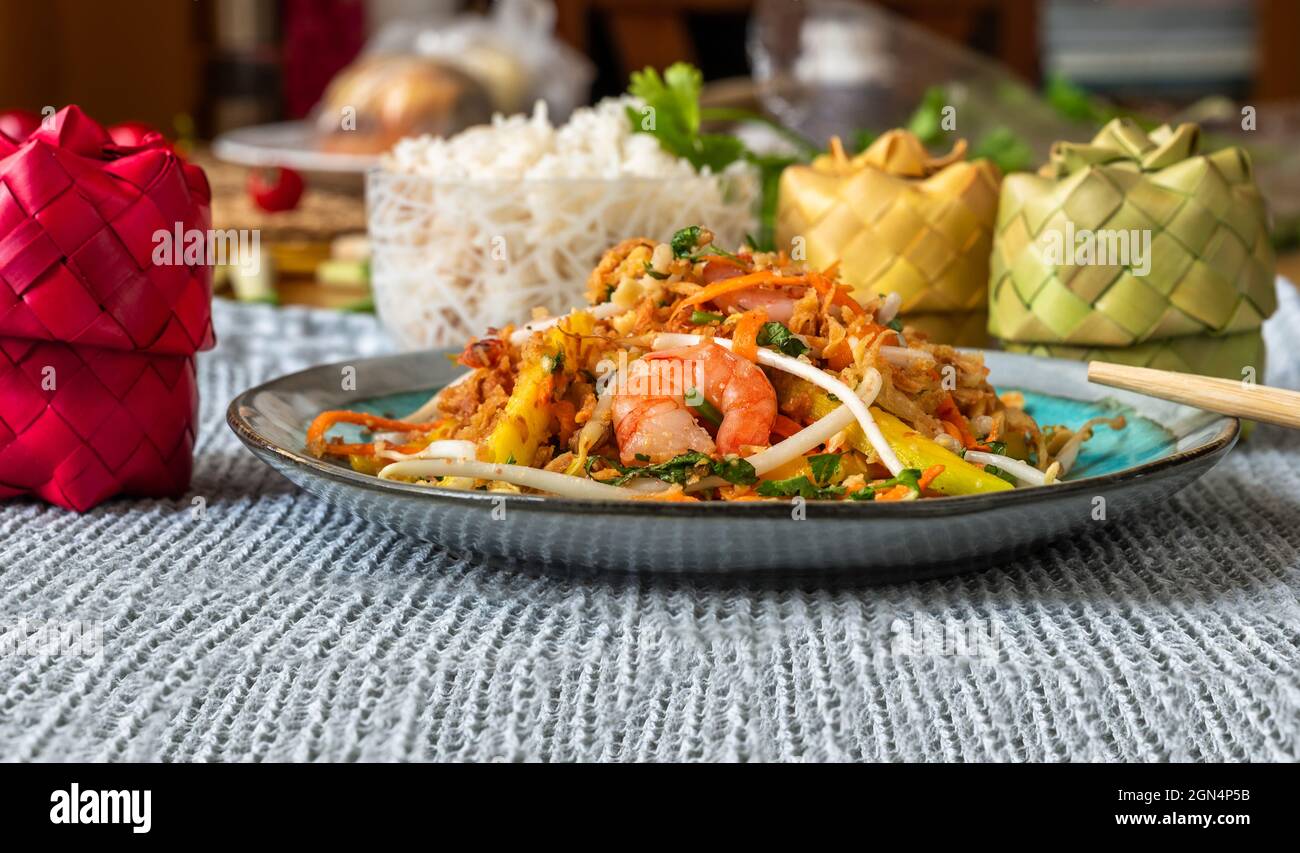 Vietnamesischer Mangosalat auf dem Teller, Reis in einer Schüssel und 3 Bambusschachtel mit Gewürzen auf dem Tisch. Stockfoto
