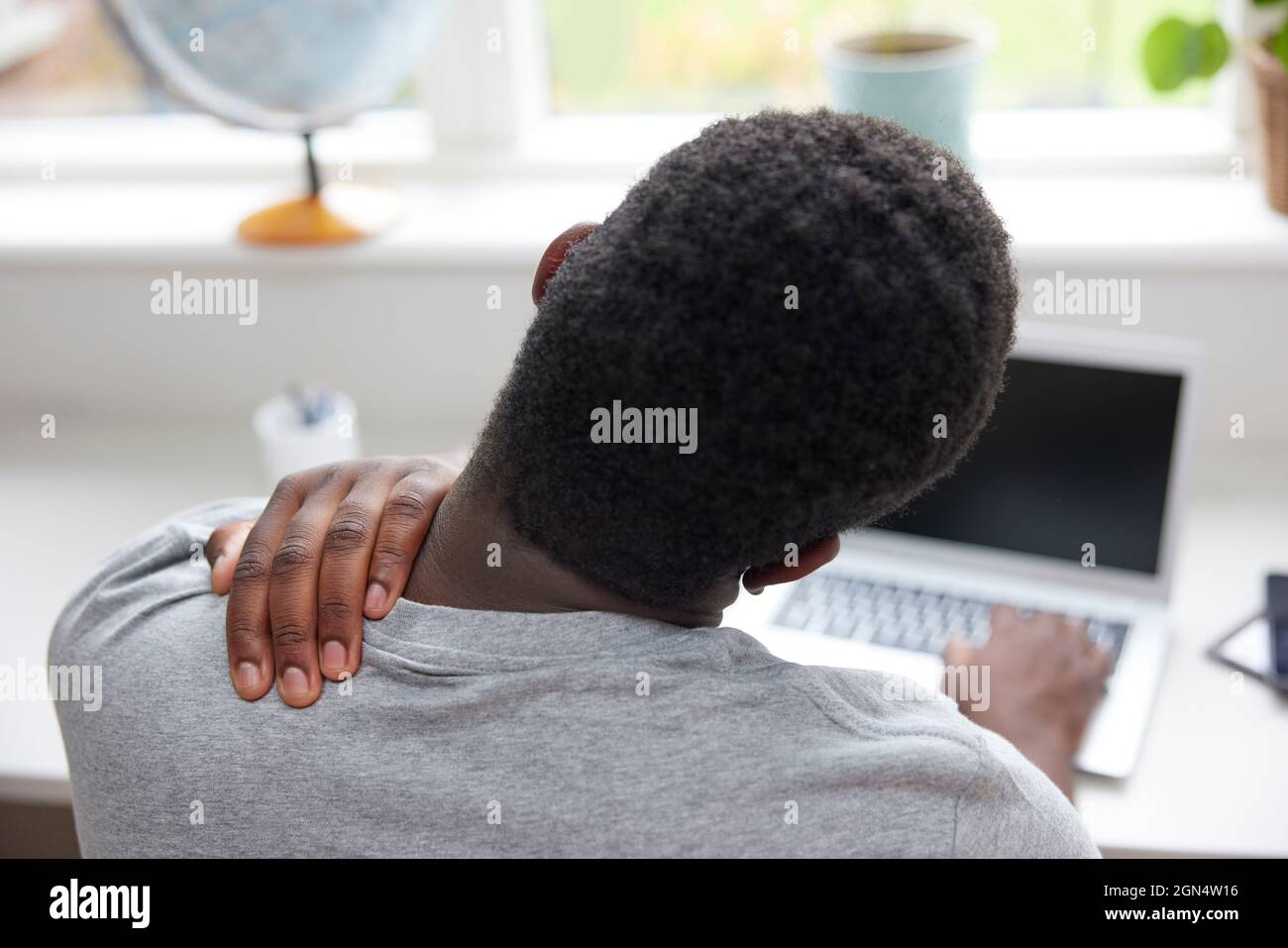 Rückansicht des Mannes zu Hause, der mit dem Laptop arbeitet, der sich Hals und Schuber vor Schmerzen reiben kann Stockfoto
