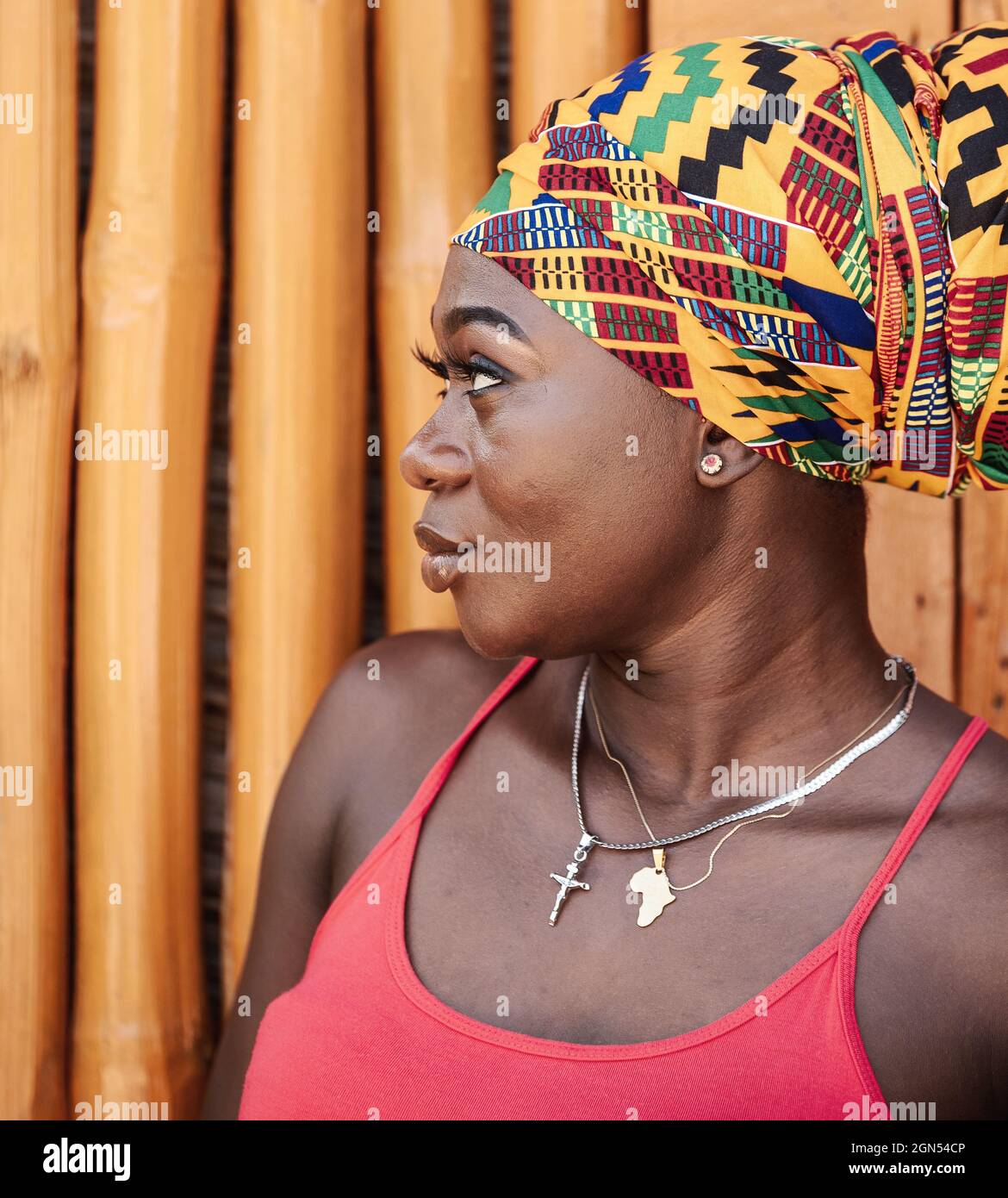 Afrikanische Frau im Profil und traditioneller Kopfschmuck, die im tropischen Dorf Keta Ghana, Westafrika, an einer bemalten Bambuswand steht Stockfoto