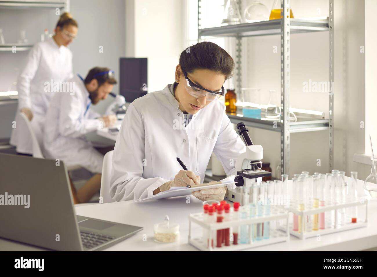Junge Wissenschaftlerin, die sich Notizen gemacht hat, während sie im modernen mikrobiologischen Labor arbeitet Stockfoto