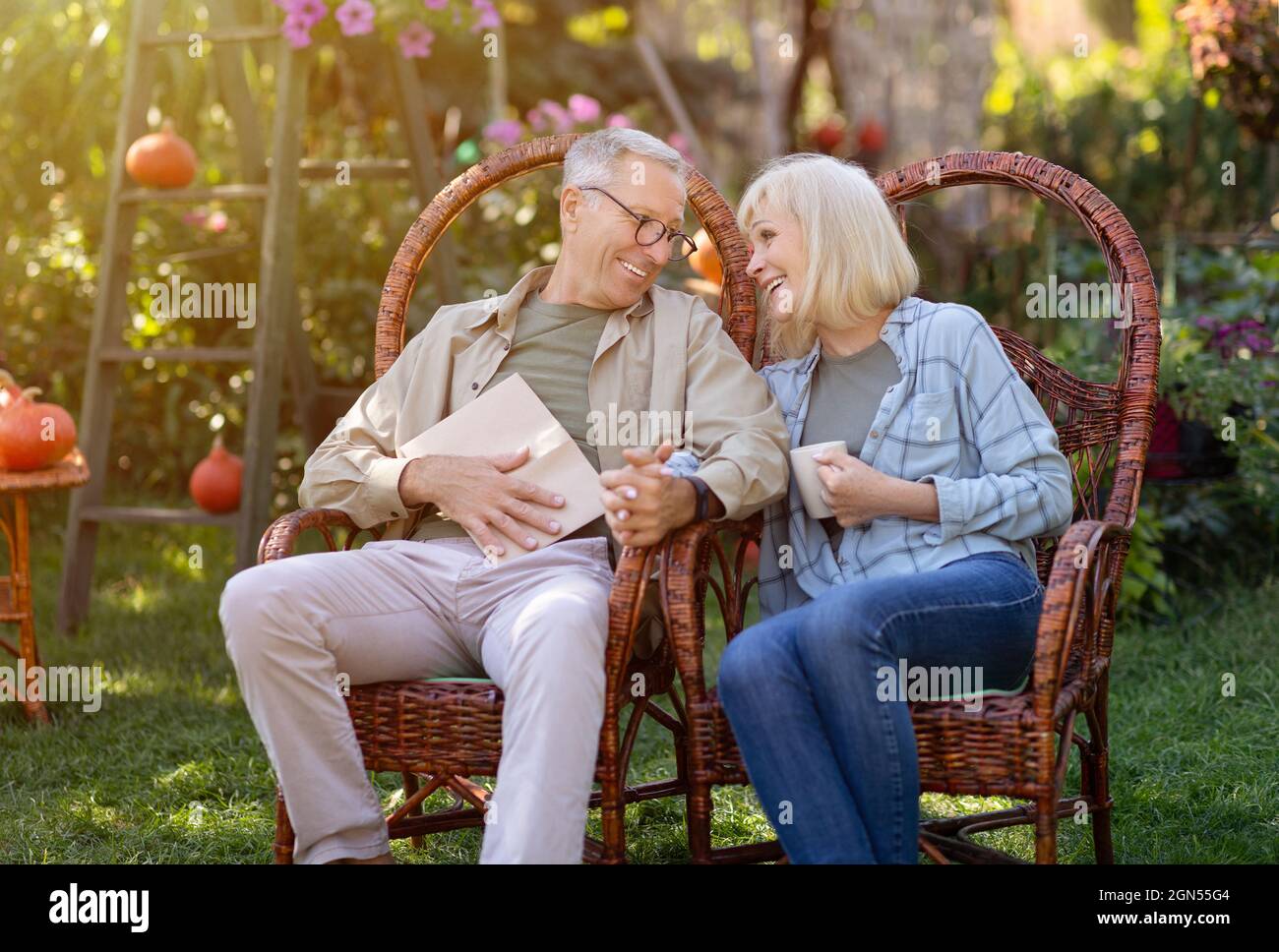 Liebende ältere Ehepartner, die sich im Garten ausruhen und warme Herbsttage genießen, in Korbstühlen im Freien sitzen, Platz zum Kopieren Stockfoto
