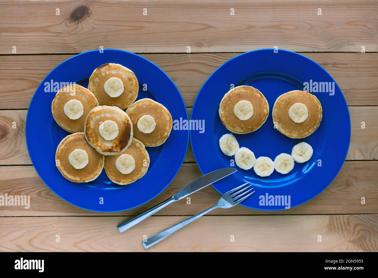 Pfannkuchen mit Lächeln auf blauem Teller und Holzhintergrund. Banana Fruit Smiling Frühstück - Spaß Essen für Kinder Stockfoto
