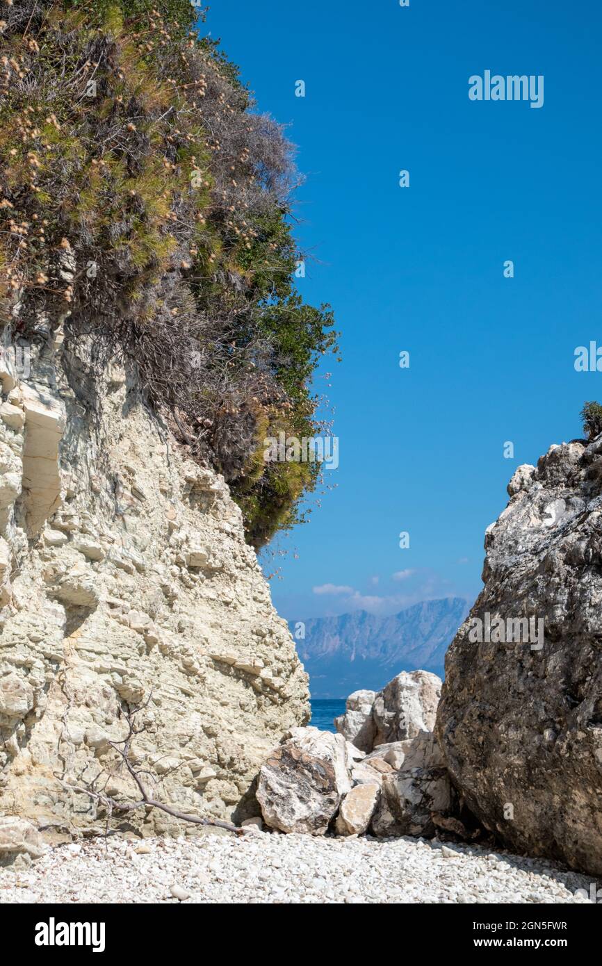 Weiße Felsen vertikale Klippe mit mediterranem Grün und blauem klaren Himmel auf Kiesstrand an der Küste der Insel Lefkada in Griechenland. Sommer wilde Natur tr Stockfoto