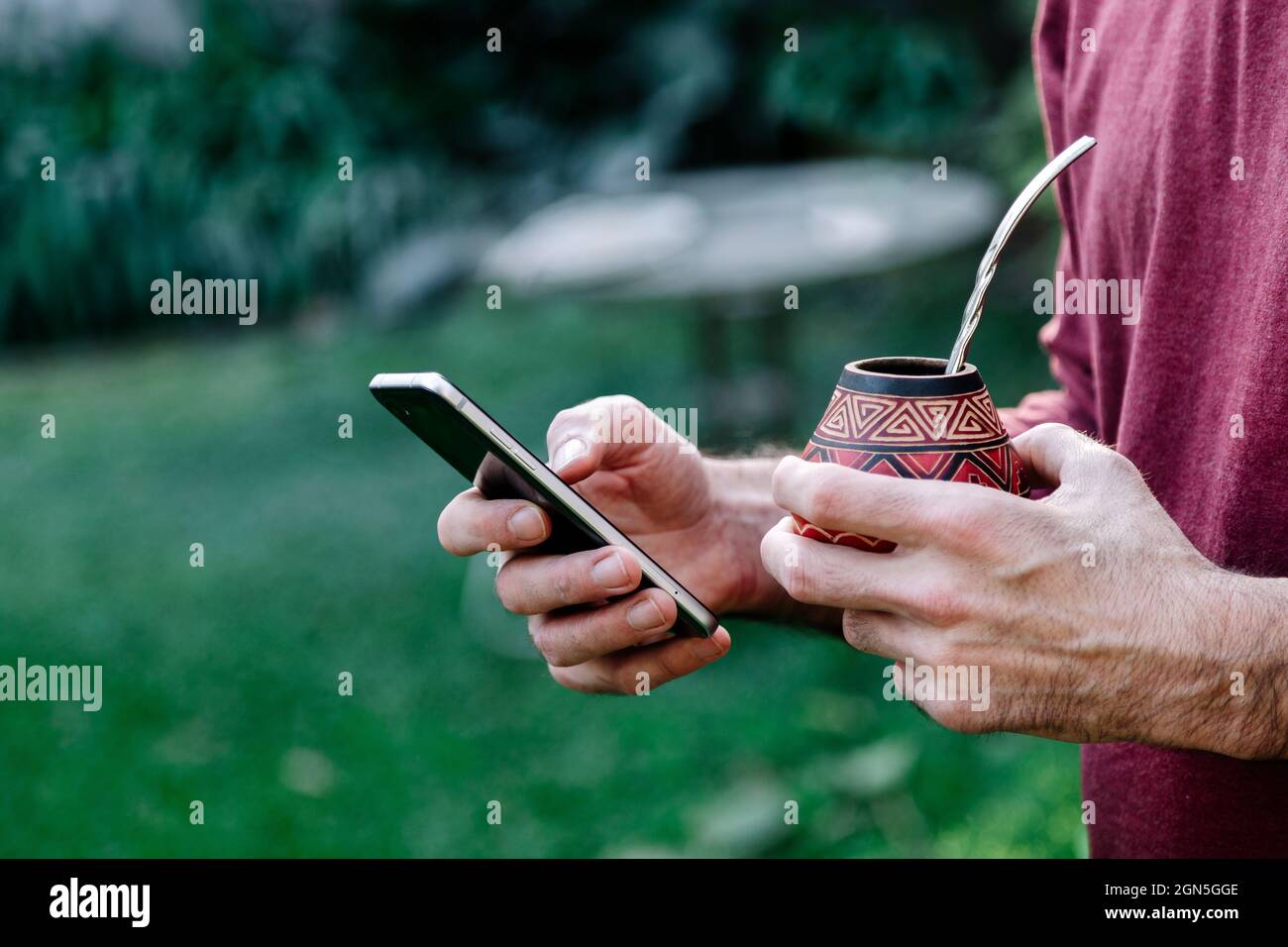 Mann mit einem Mate in der Hand und einem Handy in der anderen. Mate Tee aus Südamerika. Stockfoto