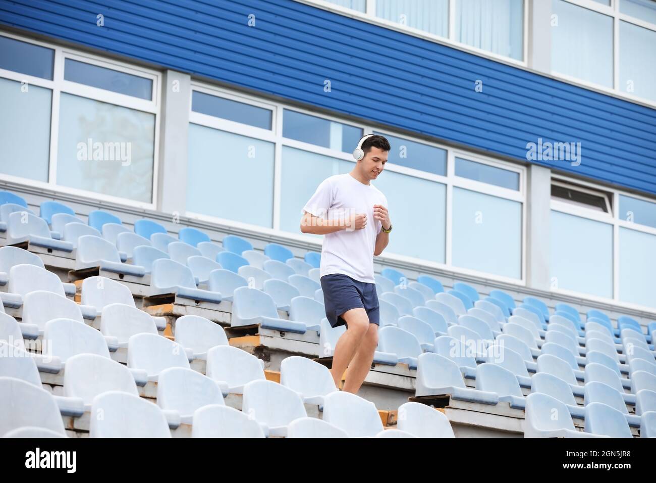 Sportlicher junger Mann mit Kopfhörern, der im Stadion unten läuft Stockfoto