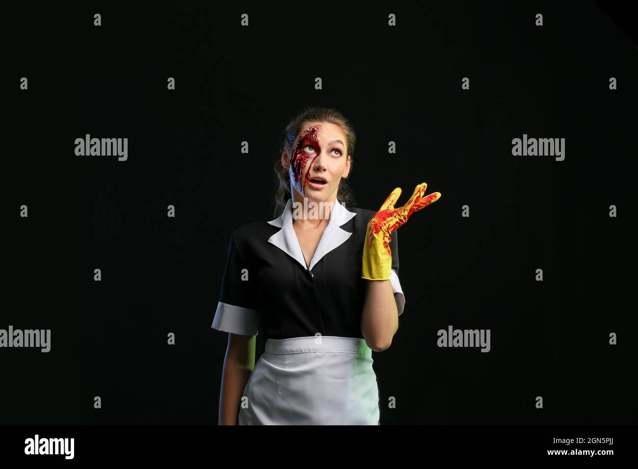 Frau, die zu Halloween als Zimmermädchen gekleidet war und etwas auf dunklem Hintergrund zeigte Stockfoto