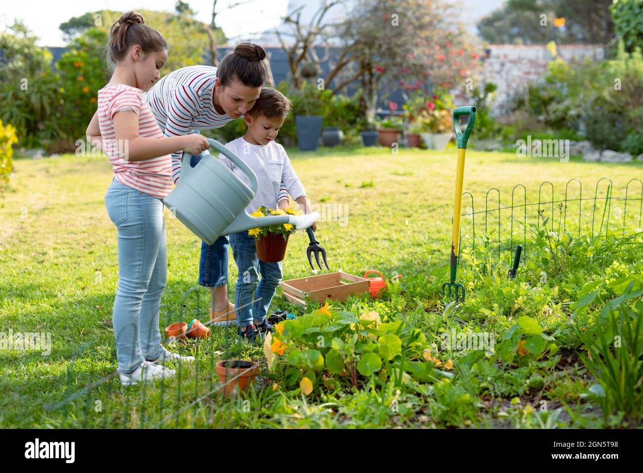 Glückliche kaukasische Mutter, Tochter und Sohn Pflanzen zusammen gießen Stockfoto