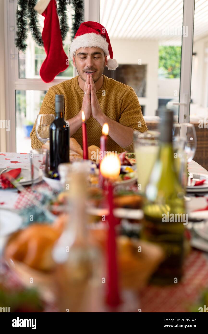 Kaukasischer Mann mit weihnachtsmütze, der am weihnachtstisch betet Stockfoto