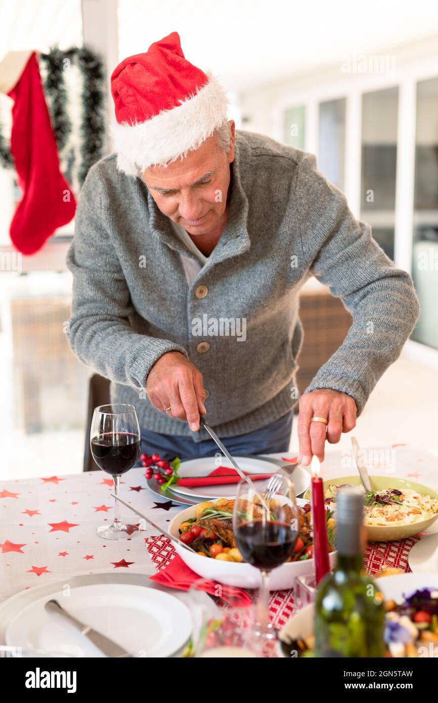 Glücklicher kaukasischer älterer Mann, der am weihnachtstisch Essen schneidet Stockfoto