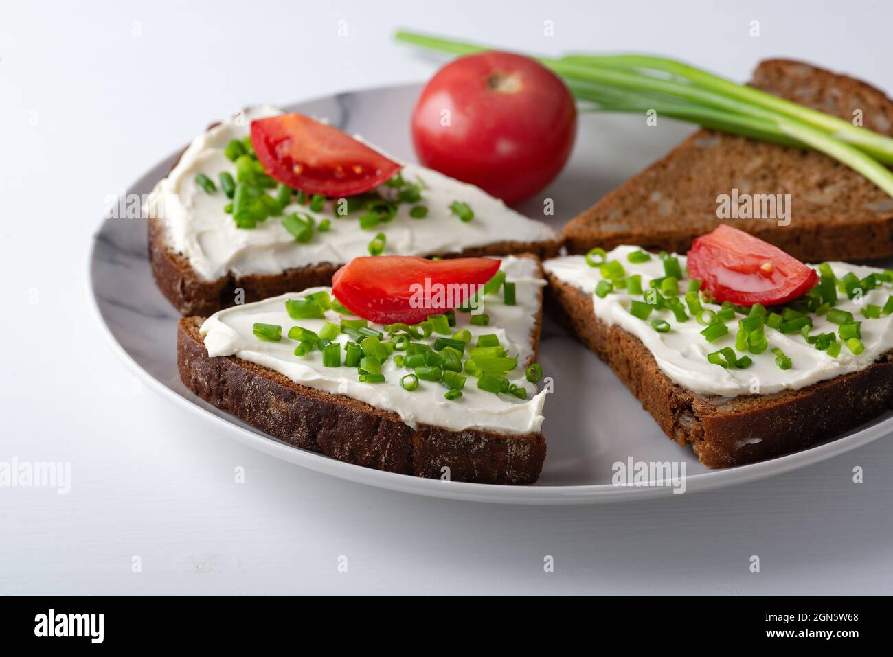 Brotscheiben mit Quark, Zwiebeln und Tomaten auf dem Teller Stockfoto