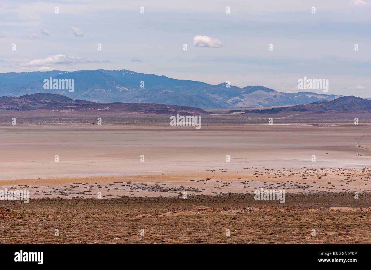 High Desert, Nevada, USA - 17. Mai 2011: Weite Landschaft mit flachem beigefarbenem trockenem See mit Bergrücken im Hintergrund unter grauer Wolkenlandschaft. Stockfoto