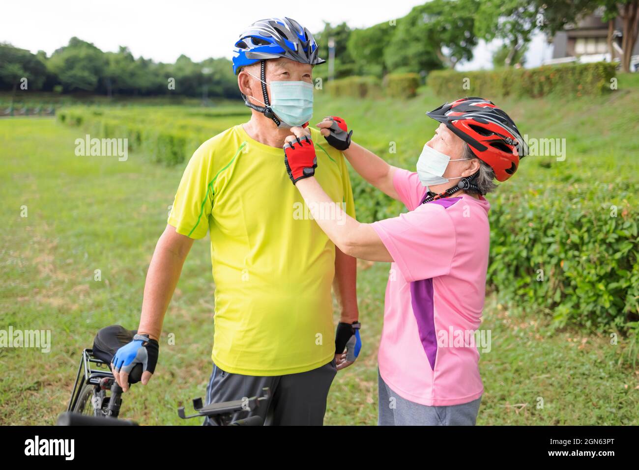 Seniorenpaar trägt medizinische Maske und fährt Fahrrad im Park Stockfoto