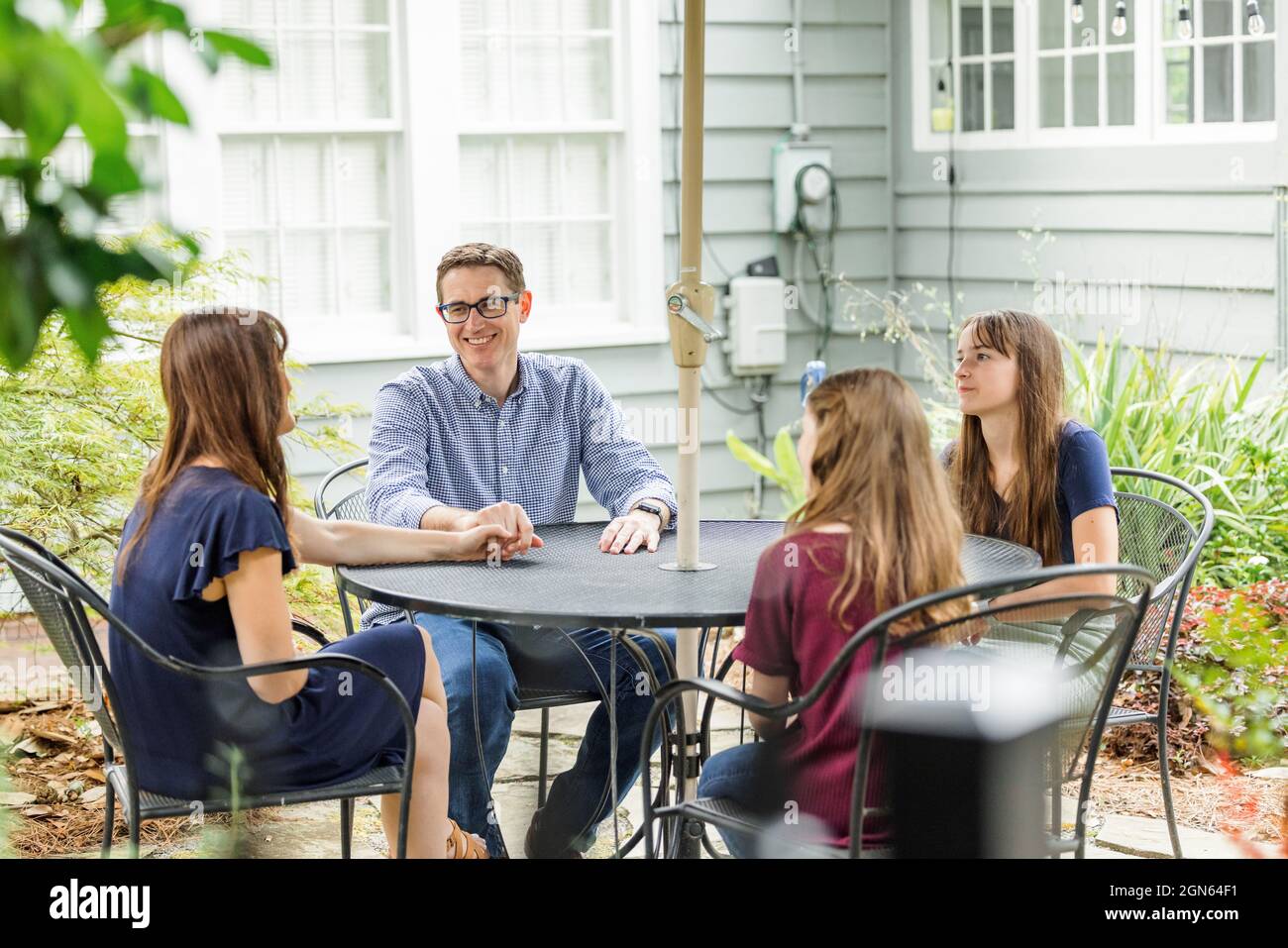 Eine Familie aus Mutter und Vater und zwei Töchtern, die draußen an einem Tisch mit Sonnenschirm sitzen Stockfoto
