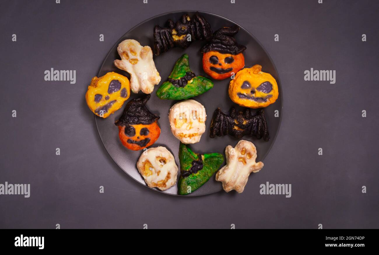 Schritt-für-Schritt Zubereitung von Hüttenkäse-Muffins für Halloween. Süße Cupcakes mit Monstern für Kinder auf einem schwarzen Teller. Farbige Kürbisse, Schädel Stockfoto
