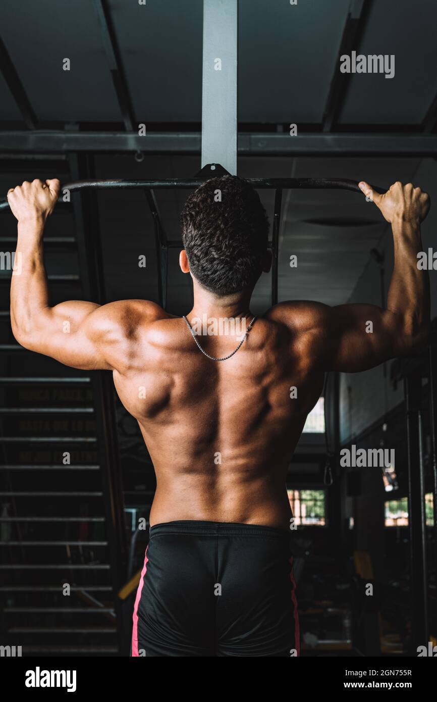 Vertikales Foto des Rückens eines starken Mannes, der in einer Turnhalle Pull-ups macht Stockfoto