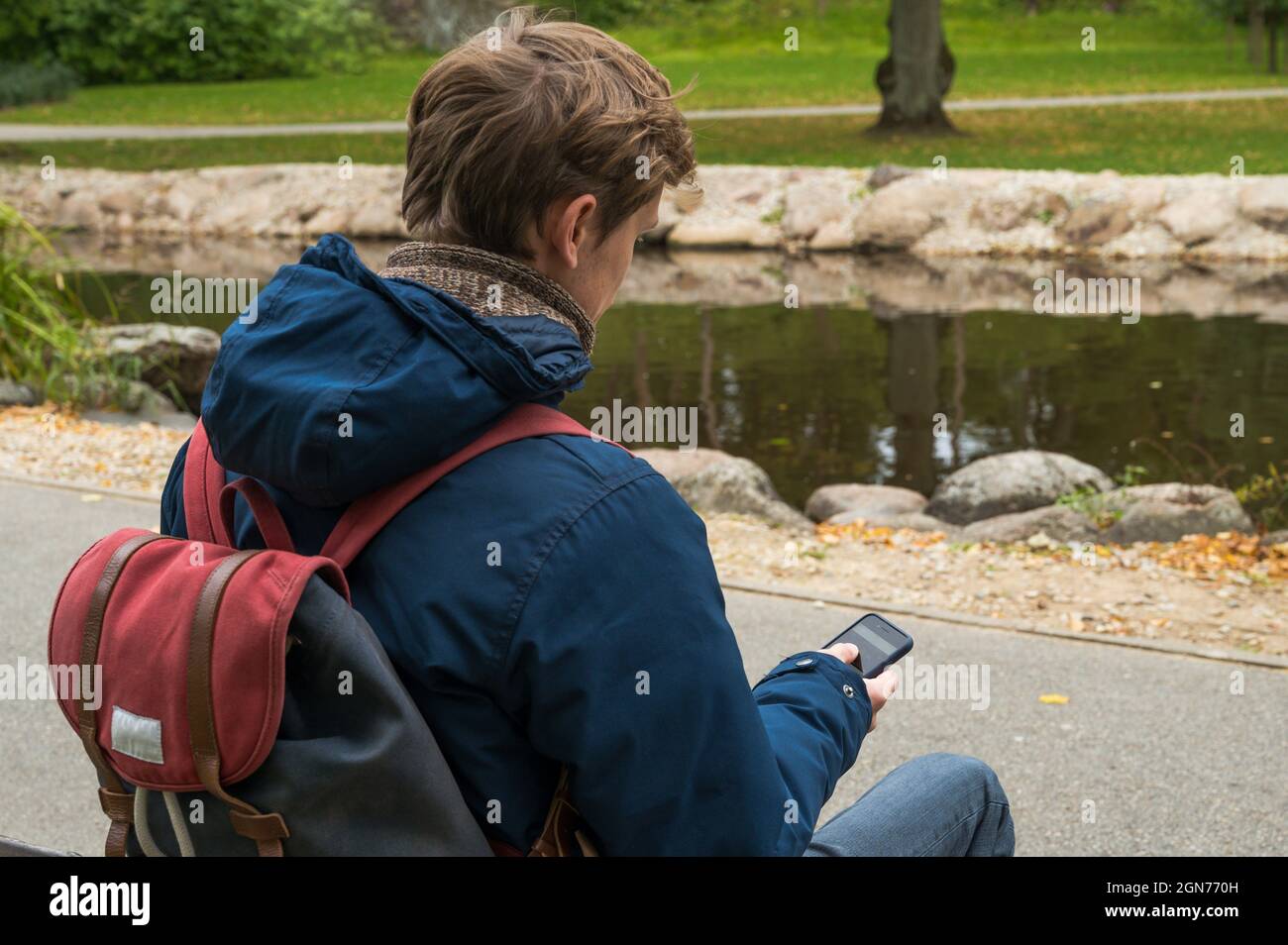 Der Mann im Herbstpark sitzt auf der Bank und hält das Telefon in der Hand. Blick von hinten. Stockfoto