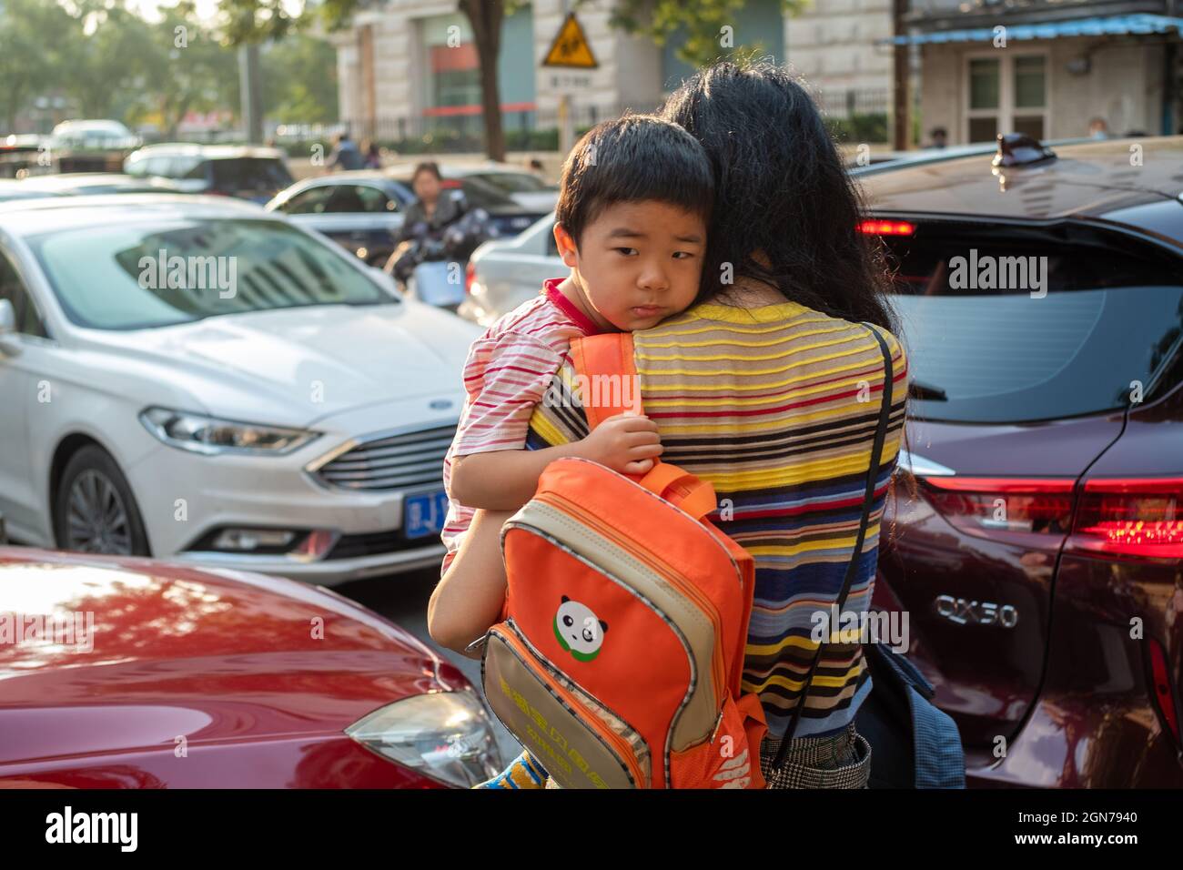 Eine chinesische Mutter hält ihren Sohn fest und geht am Morgen in Peking, China, durch eine Gruppe blockierter Privatwagen zu seinem Kindergarten. 23-Sep-2012 Stockfoto