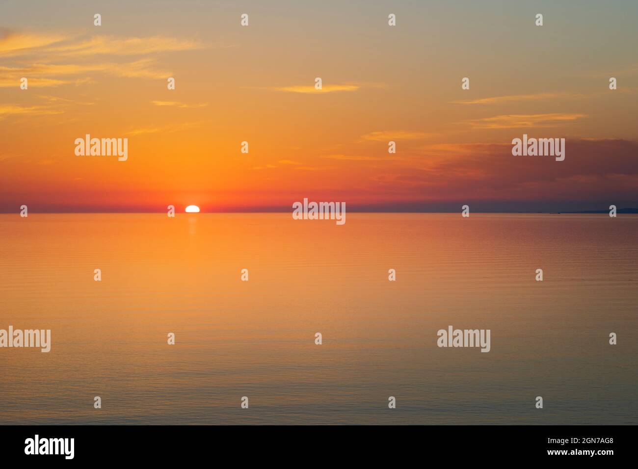 Die Sonne geht bei Sonnenuntergang über einem ruhigen Meer unter Stockfoto