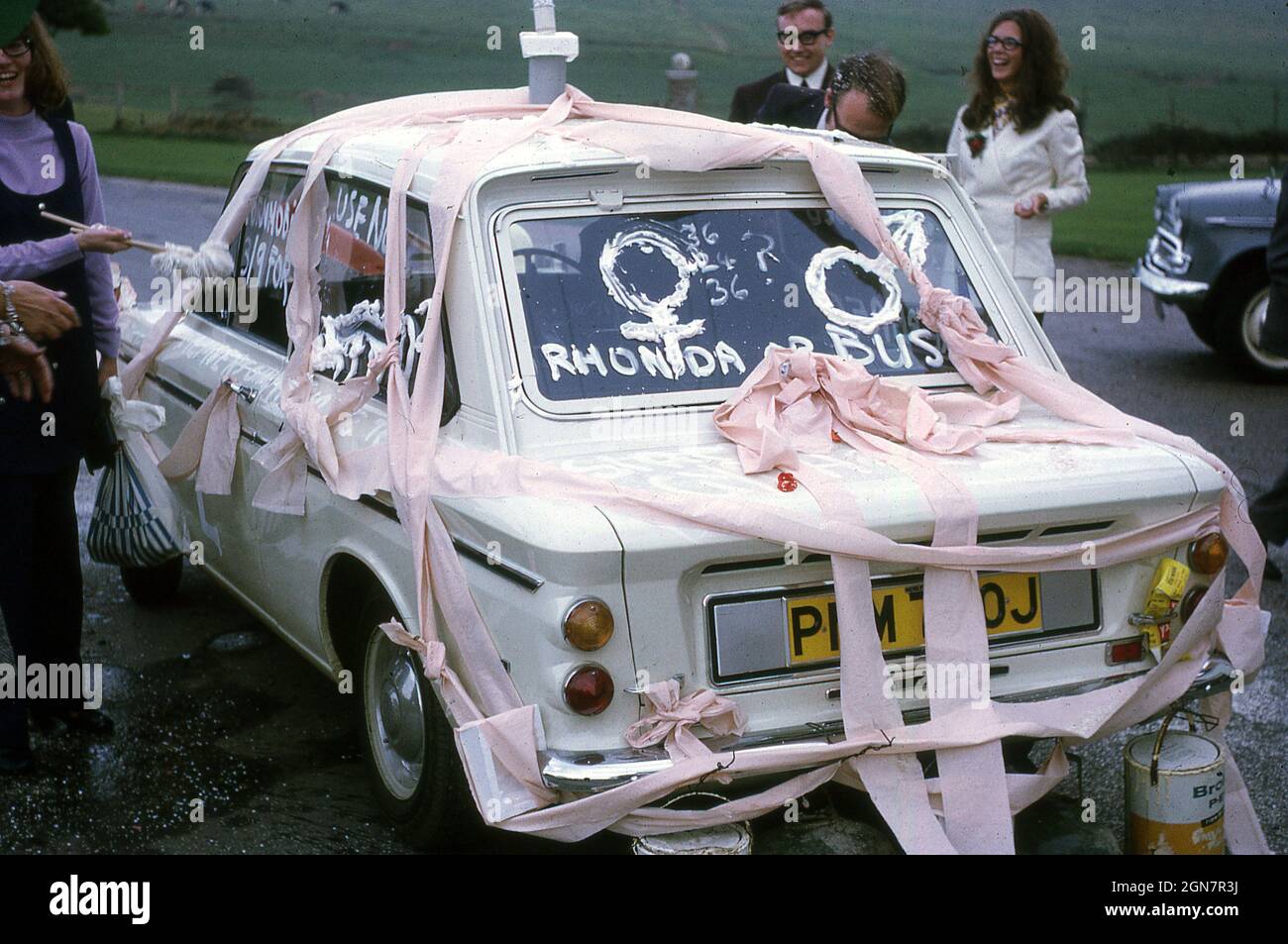 1970, November, ein geschmückter Hochzeitswagen, ein weißer Hillman Imp, mit pinken Bändern und Blechdosen, die an der hinteren Stoßstange befestigt sind, mit Schriftzug auf der hinteren Windschutzscheibe, Rhonda oder Bust, England, Großbritannien. Stockfoto