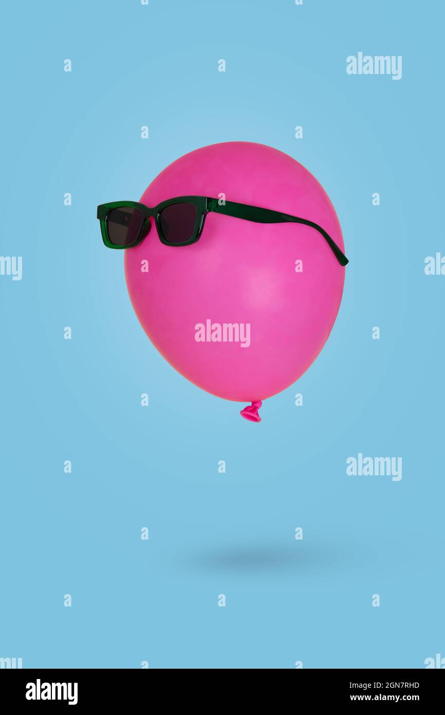 Pinkfarbener Ballon in Sonnenbrillen, der vor blauem Hintergrund in der Luft schwebt. Minimal Kreativität und Glück Konzept . Gute Party-Stimmung Stockfoto