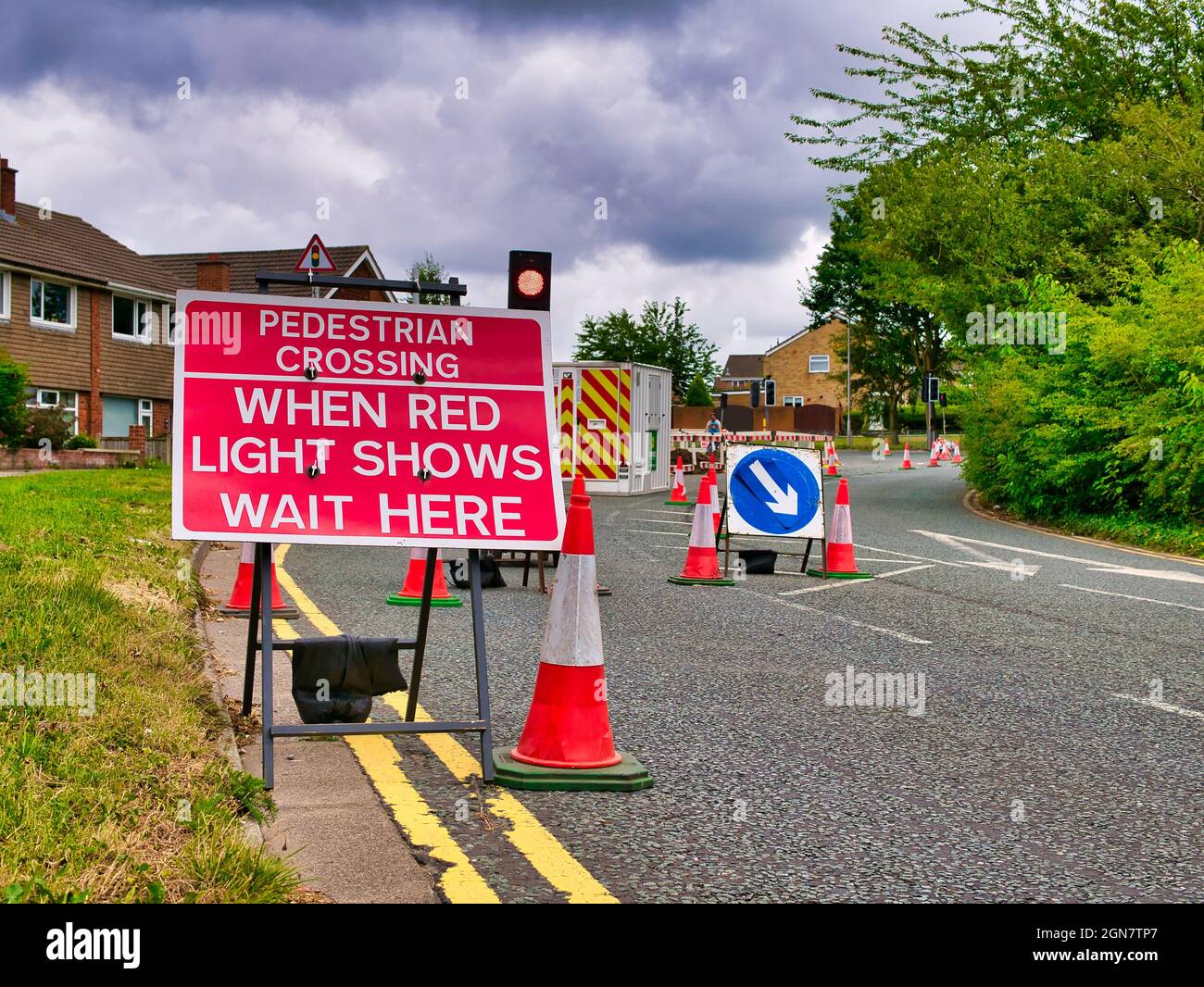 Ein rotes Schild mit weißer Beschriftung weist Autofahrer darauf hin, dass vor den Bauarbeiten eine Fußgängerüberfahrt liegt und das an einer Leselampe warten sollte. Stockfoto