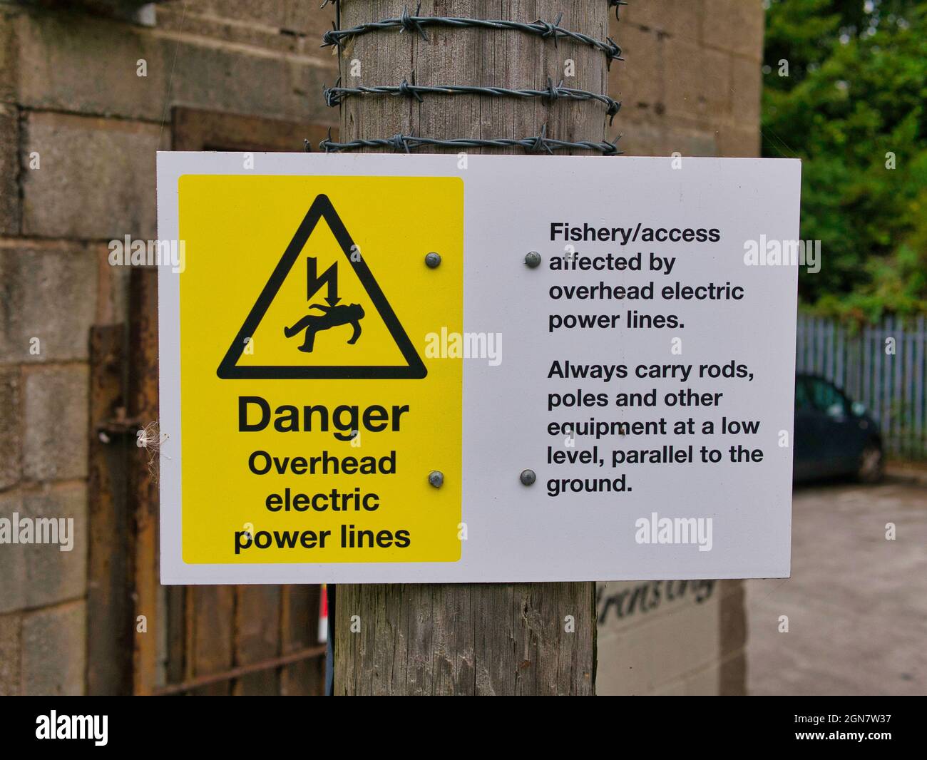 Ein gelb-weißes Gefahrenschild auf dem Leeds-Liverpool-Kanal in Lancashire, Großbritannien, warnt Angler vor Stromleitungen über dem Kopf. Stockfoto