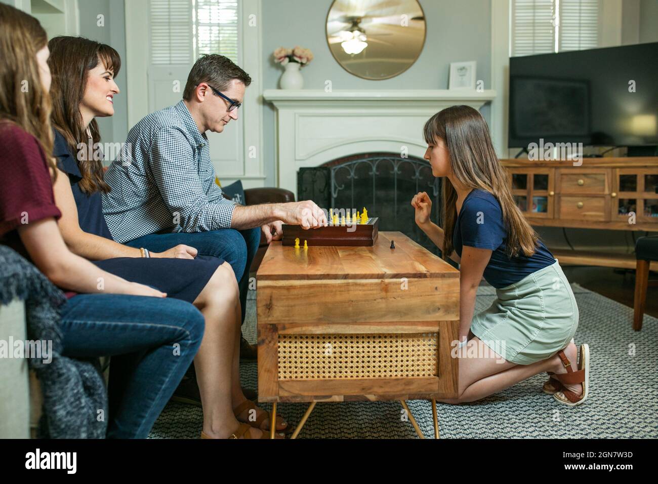 Eine vierköpfige Familie mit Mutter, Vater und zwei Töchtern, die auf einer Couch sitzen und Schach spielen, um am Familienspiel-Abend teilzunehmen Stockfoto