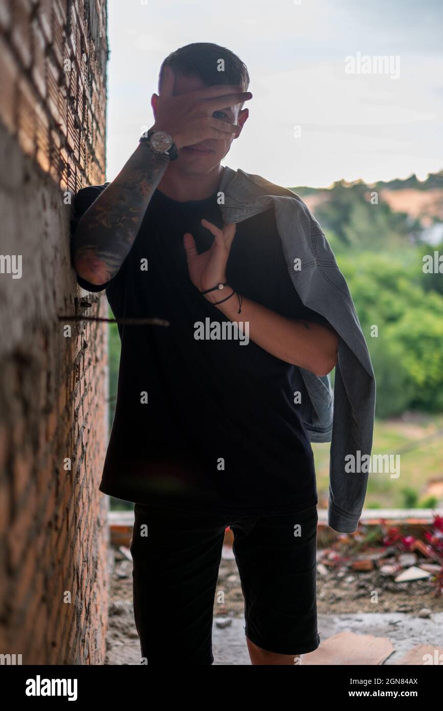 Porträt eines jungen hübschen kaukasischen Mannes in lässiger schwarzer Kleidung, der durch die Finger schaut. Blick auf die Kamera. Jacke mit HalteDenim Stockfoto