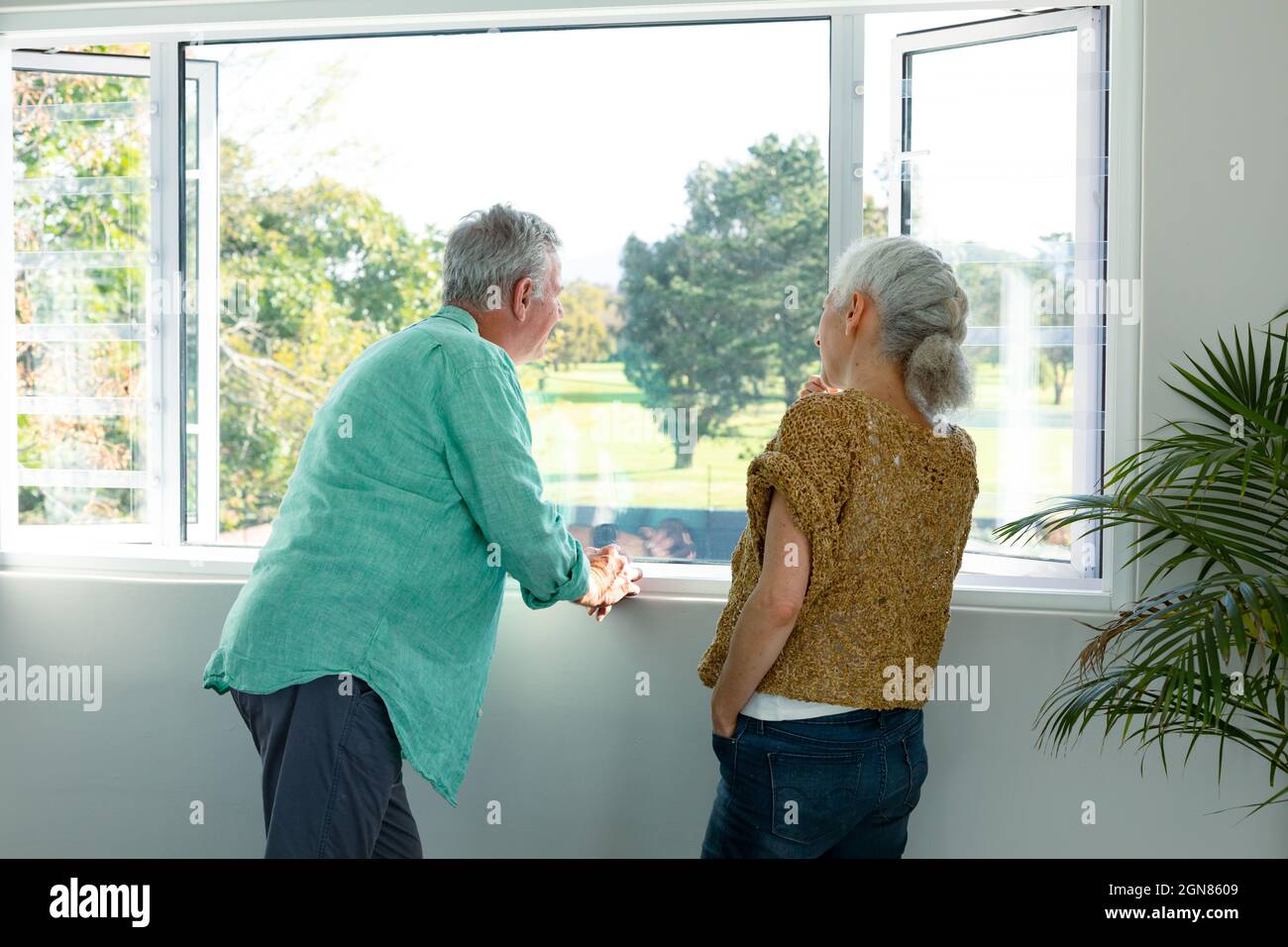 Rückansicht des kaukasischen älteren Ehepaares, das am Fenster stand und redete Stockfoto