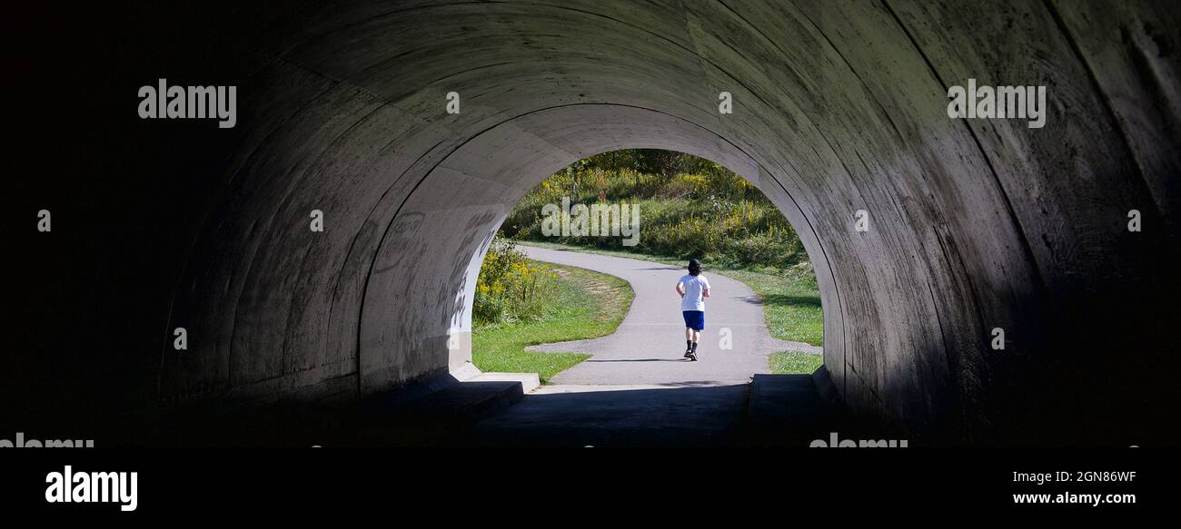 Blick auf einen dunklen Tunnel im öffentlichen Park mit einem Läufer Stockfoto
