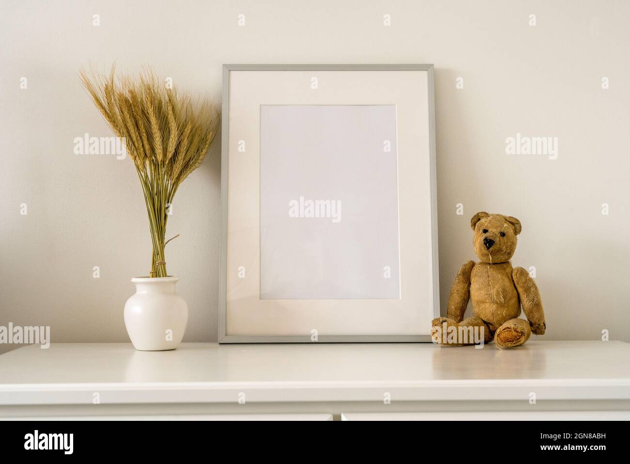 Silberner Fotorahmen mit Innenmock mit Vase mit getrockneten Weizenohren und einem antiken Teddybären Stockfoto