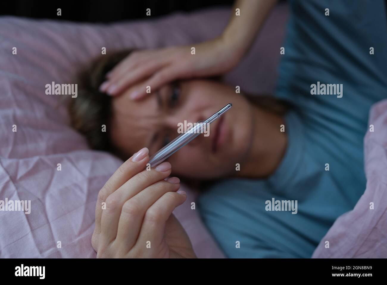 Kranke Frau, die im Bett liegt und Thermometer mit hoher Temperatur in Nahaufnahme hält Stockfoto