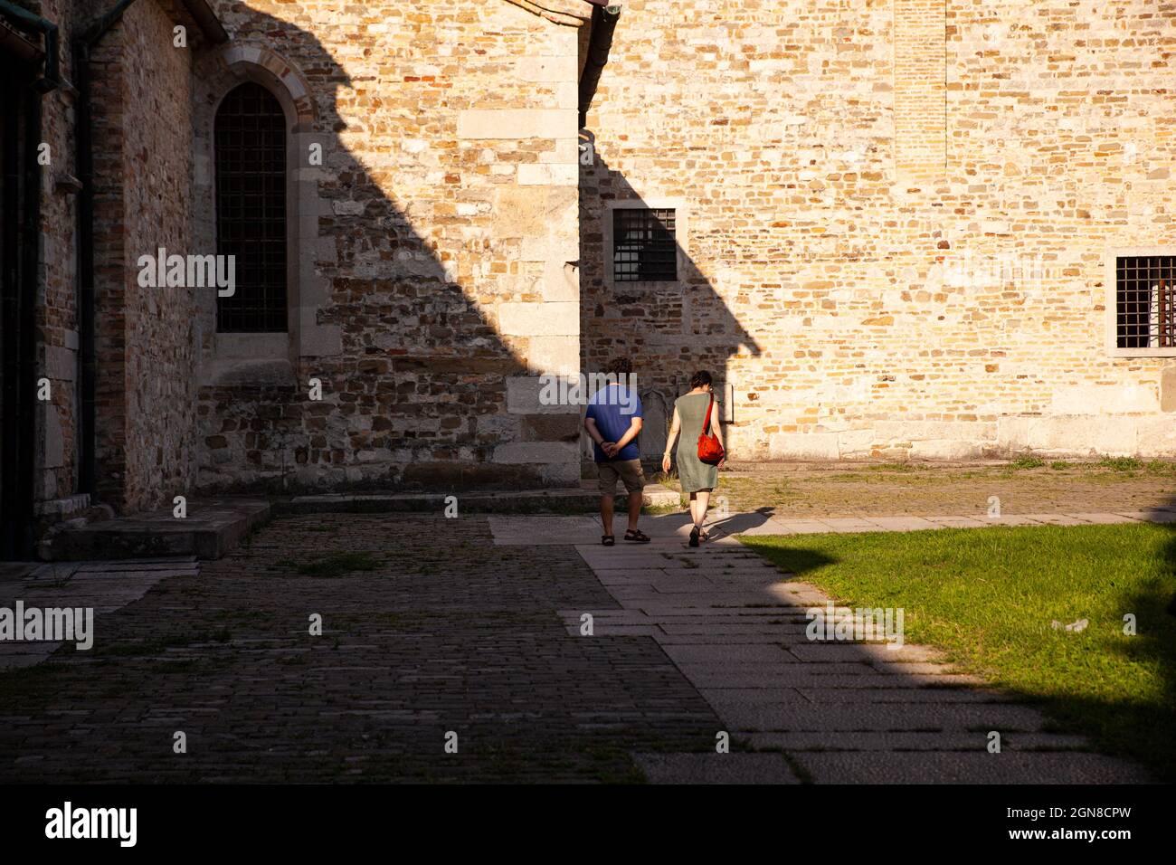 Aquileia, italien - August 15: Ein paar Touristen, die am 15. August 2021 neben der Basilika Santa Maria Assunta spazieren gehen Stockfoto