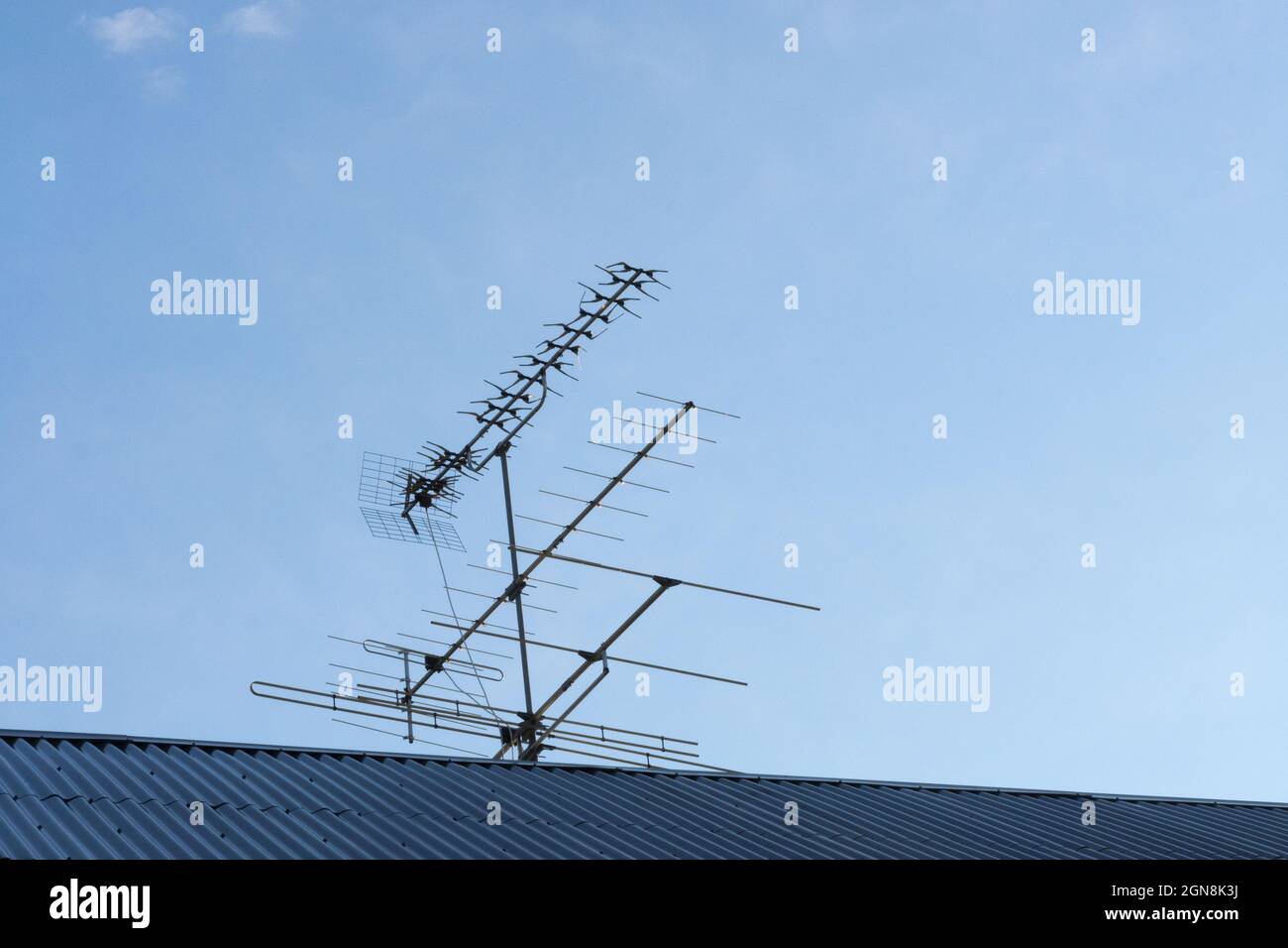 Antenne für den Empfang von Fernsehprogrammen auf einem grauen Ziegeldach gegen einen blauen Himmel Stockfoto