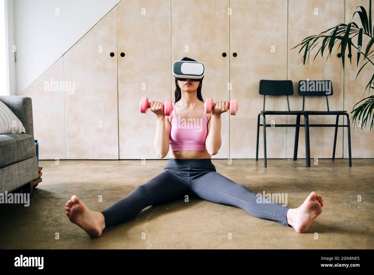 Frau, die ein Virtual-Reality-Headset verwendet, während sie zu Hause mit Kurzhanteln trainiert Stockfoto