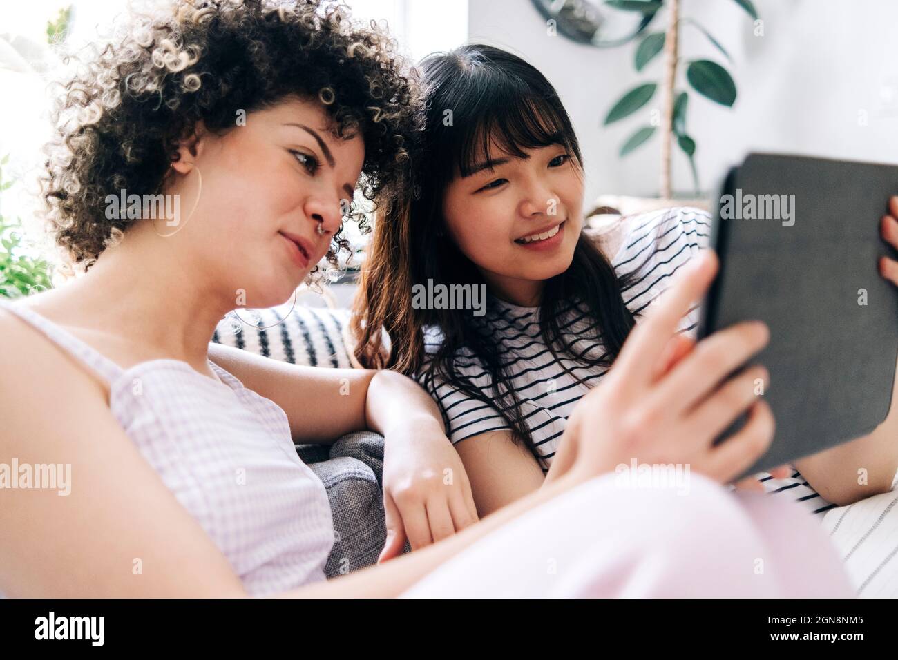 Lächelnde Frau mit einem digitalen Tablet und einer Freundin zu Hause Stockfoto
