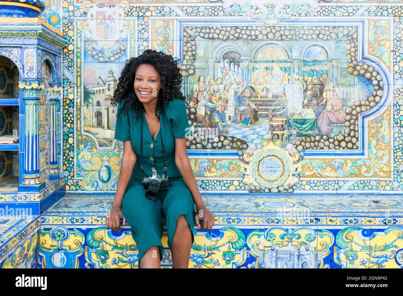 Fröhliche junge Afro-Frau mit Kamera vor dem Mosaik auf der Plaza De Espana, Sevilla, Spanien Stockfoto