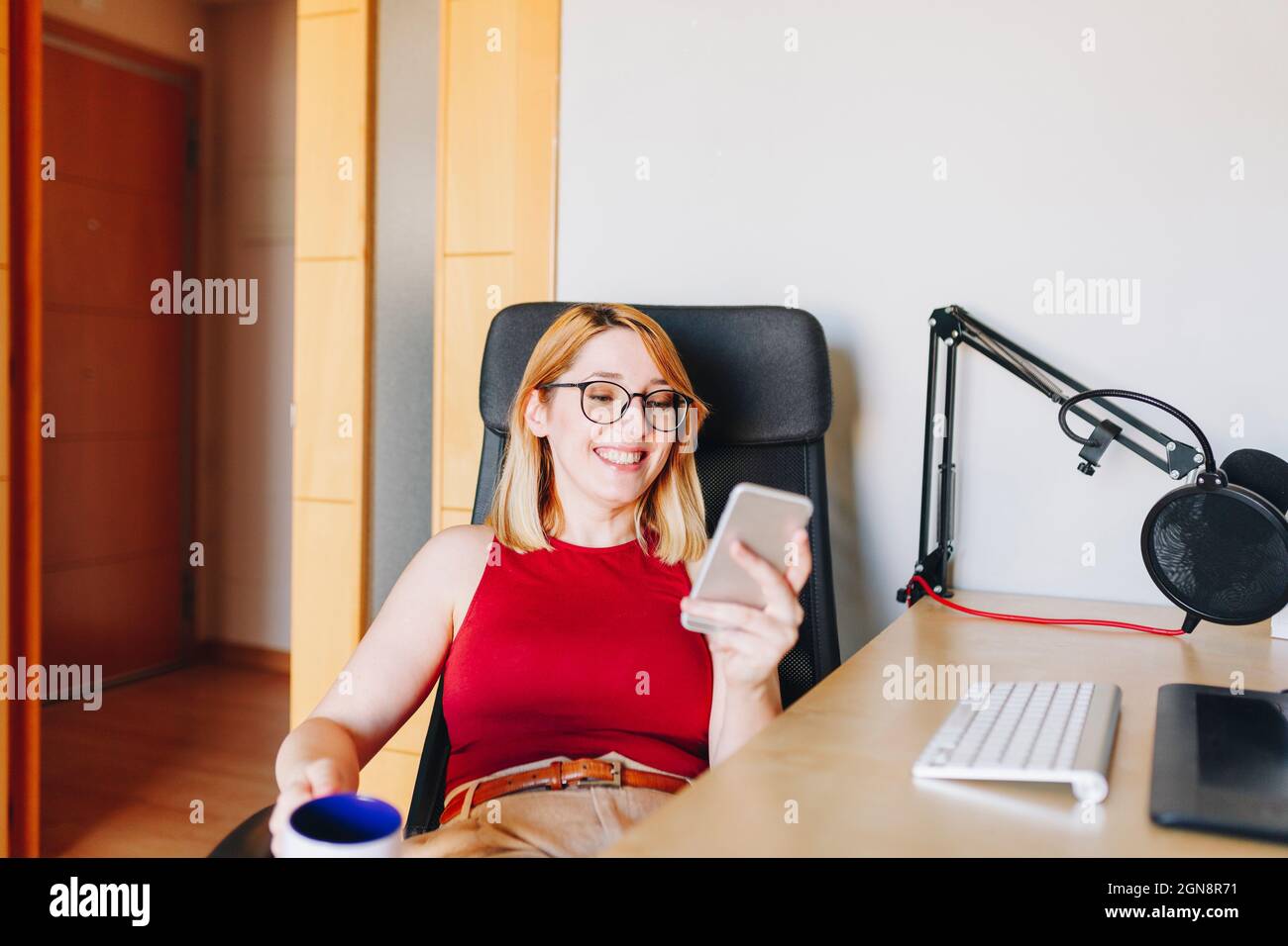 Lächelnde Geschäftsfrau mit Mobiltelefon, während sie im Heimbüro auf einem Drehstuhl sitzt Stockfoto