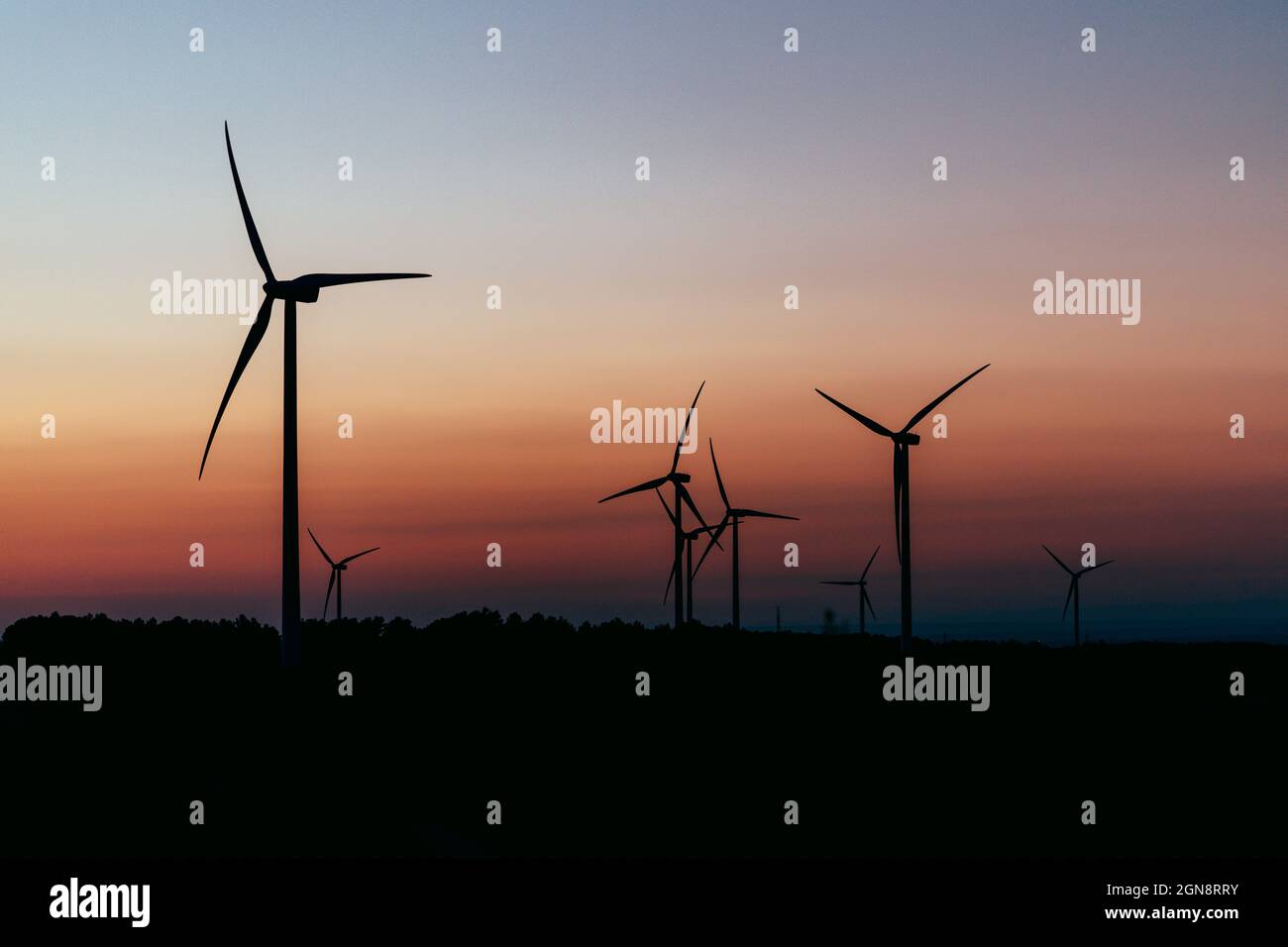 Silhouetten von Windenergieanlagen, die in der Abenddämmerung gegen den launischen Himmel stehen Stockfoto