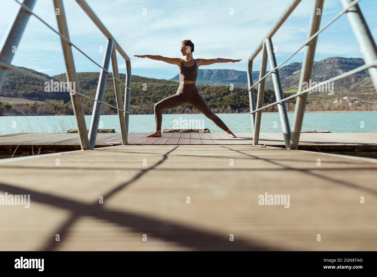 Sportlerin doing Warrior 2 Pose an sonnigen Tagen auf dem Steg Stockfoto