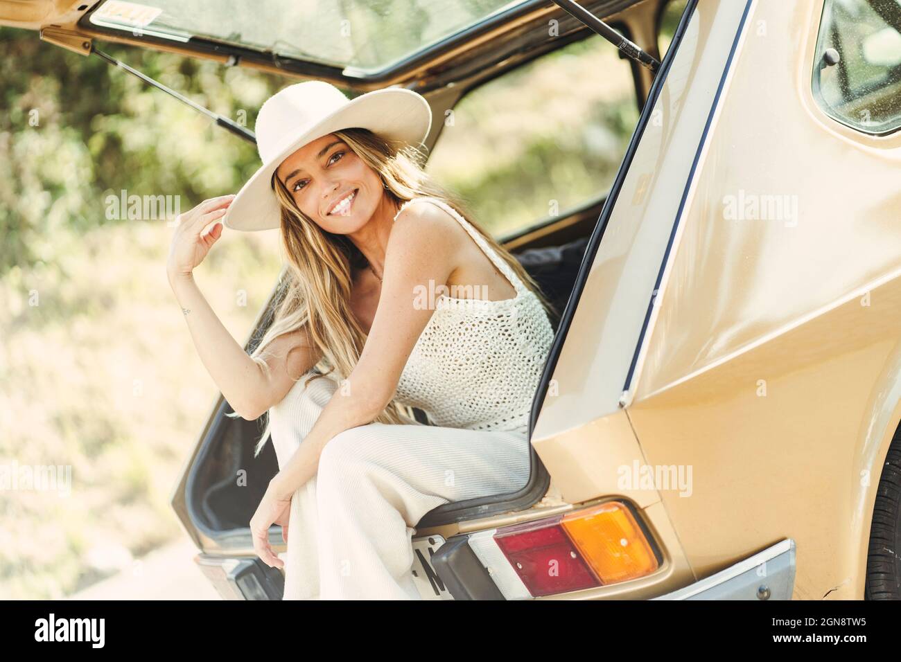 Lächelnde blonde Frau mit Hut sitzt im Kofferraum Stockfoto Lächelnde blonde Frau mit Hut sitzt im Kofferraum Stockfoto