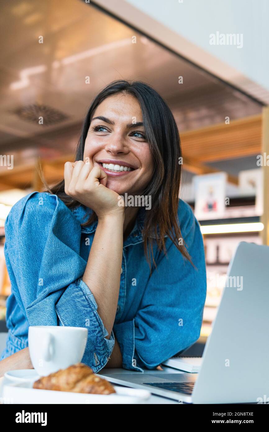 Schöne Geschäftsfrau mit der Hand auf dem Kinn, die sich im Café auf den Tisch lehnte Stockfoto