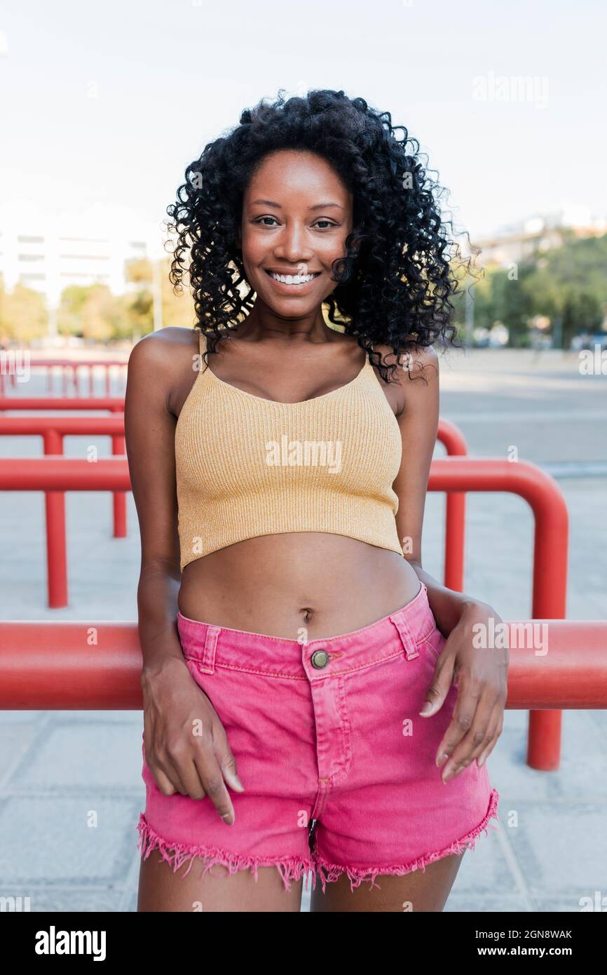 Lächelnde junge Afro-Frau, die sich auf ein rotes Geländer stützt Stockfoto