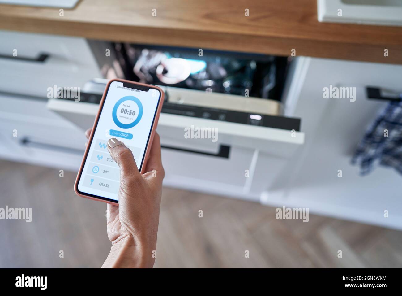 Frau, die den Geschirrspüler zu Hause mit einer mobilen Anwendung bedient Stockfoto
