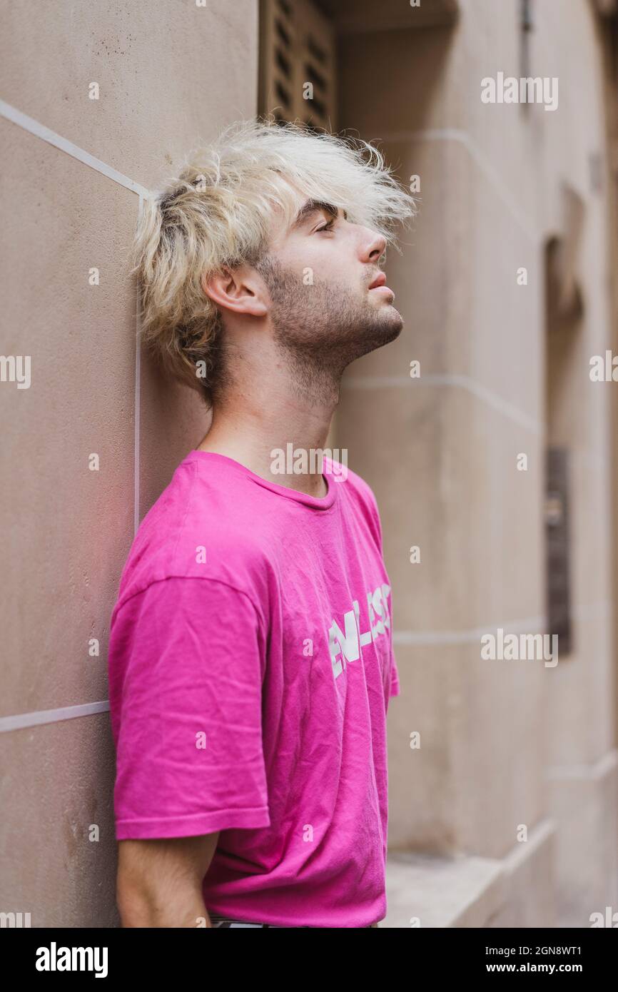 Junger Mann in pinkem T-Shirt, der sich an der Wand lehnt und kontempliert Stockfoto