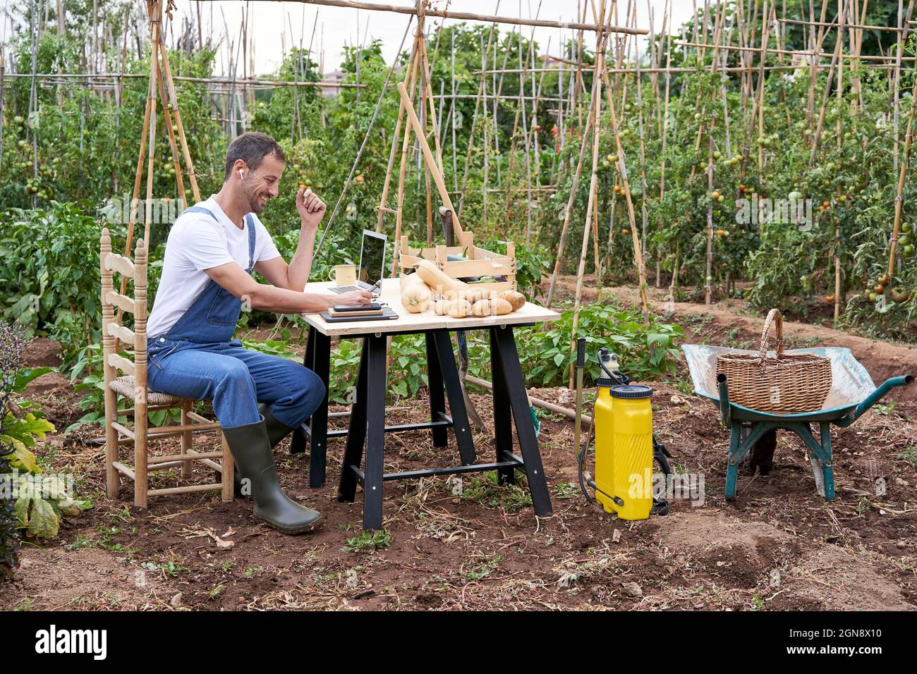 Lächelnder Bauer, der mit einem Laptop am Tisch auf dem landwirtschaftlichen Feld arbeitet Stockfoto