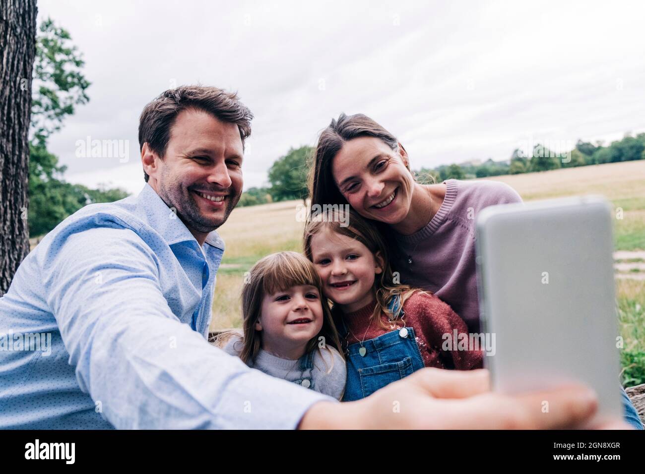 Lächelnder Vater nimmt Selfie mit der Familie über Smartphone im Park Stockfoto
