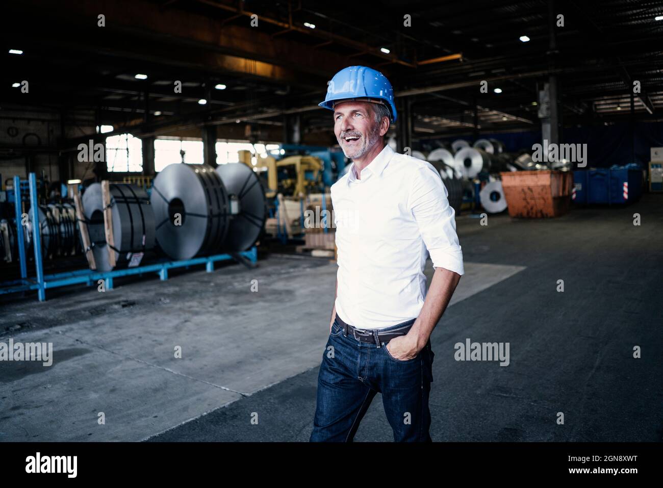 Fröhlicher männlicher Ingenieur mit der Hand in der Tasche, der in der Stahlmühle läuft Stockfoto