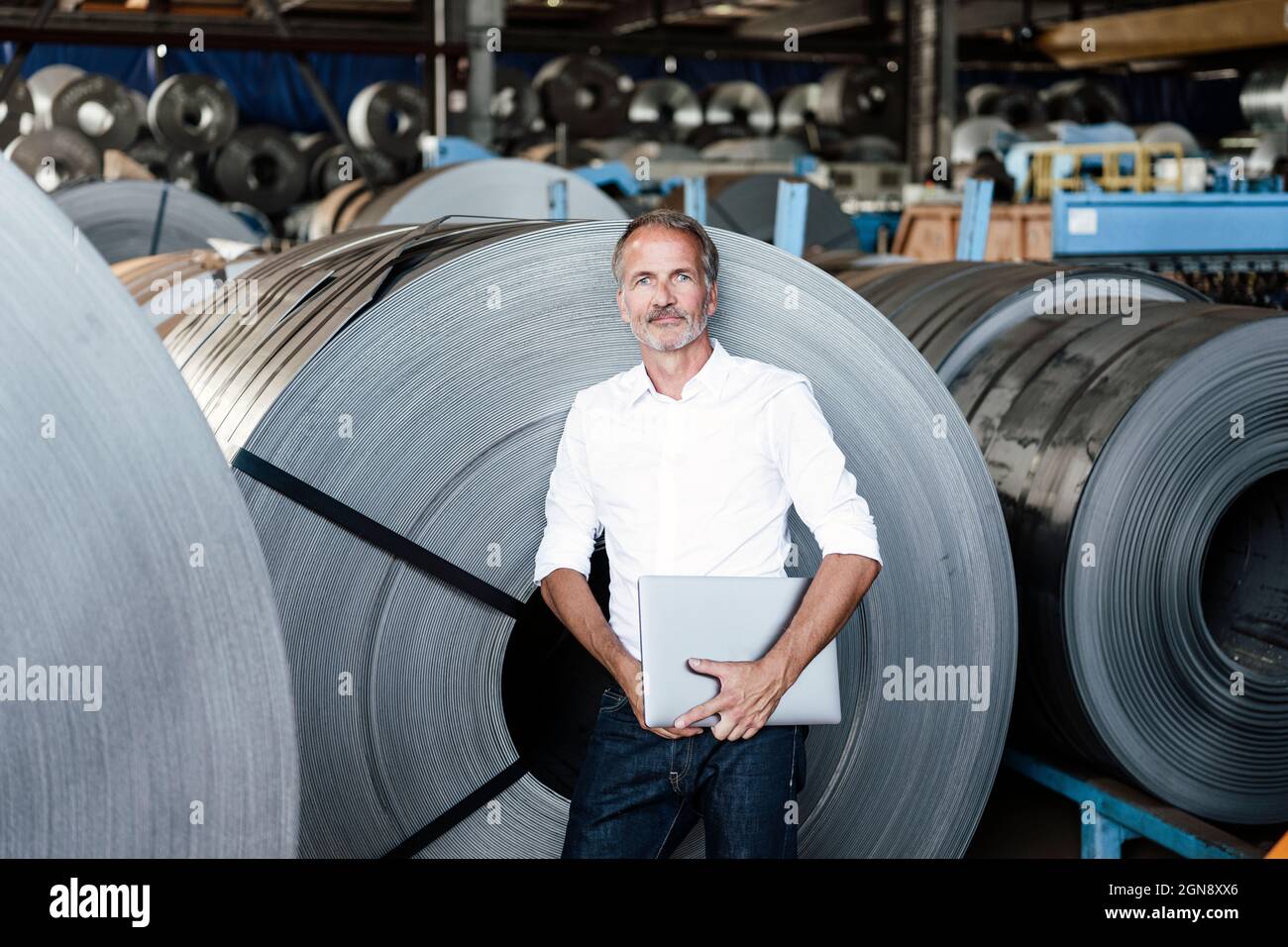 Älterer Profi mit Laptop, während er sich auf eine Blechrolle lehnte Stockfoto