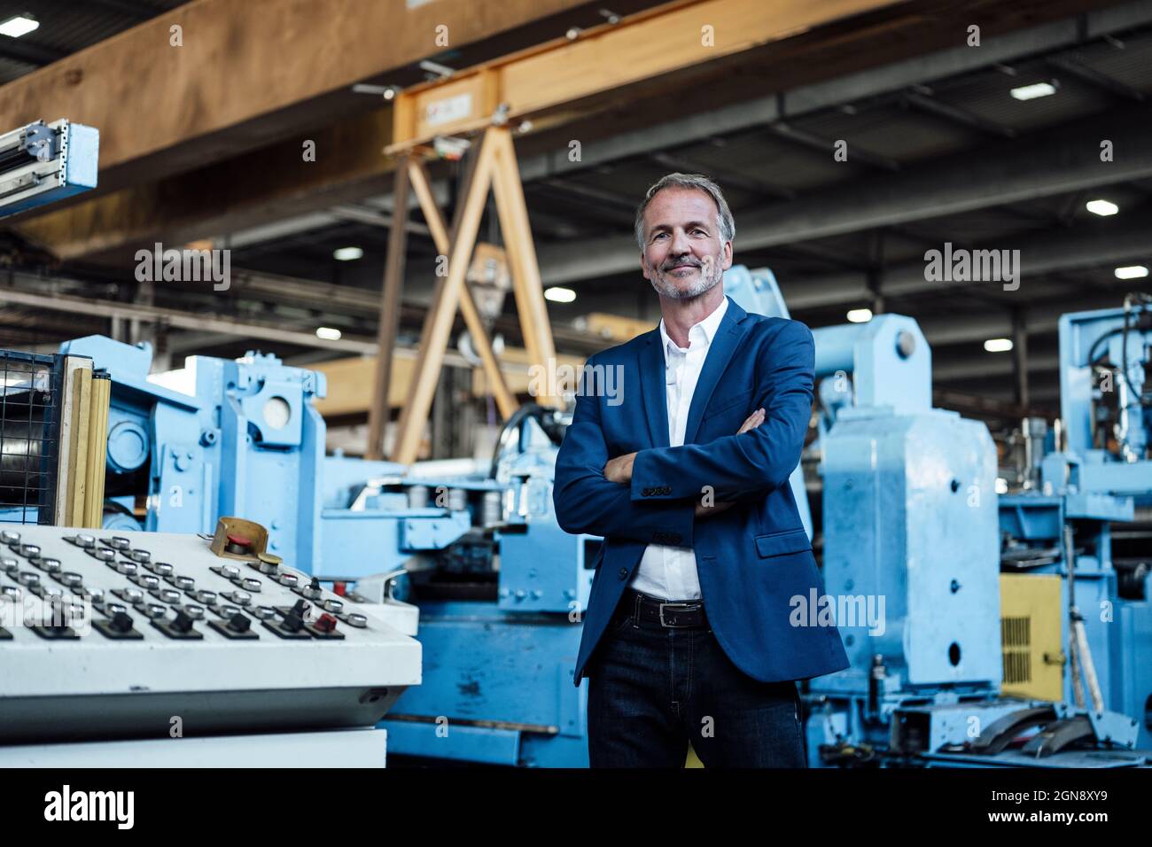 Männlicher Geschäftsmann mit gekreuzten Armen in der Metallindustrie Stockfoto